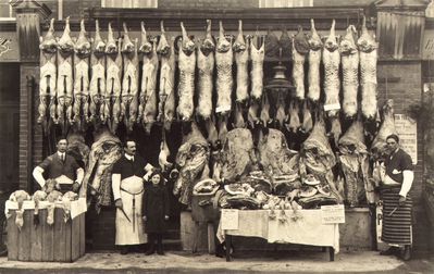 A. H. Clarke, butcher.
The poster behind the figure on the right is partly obscured, but the following wording is visible: "...thletes' ...teer Force / ... ments of rifle shooting / ... meeting / ... club hall / ... 9th 1914". 

A sales plackard reads "XMAS XMAS / ALBERT H. CLARKE / 109 ORDNANCE ROAD / having purchased a large consignment of / PIGS & POULTRY from NORFOLK / is now receiving orders for /LEGS of PORK, TURKEYS / GEESE, FOWLS &c. / PRIME OX BEEF a Speciality" 
Keywords: 1910s;butchers;shops;retail