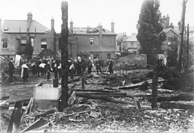 Fire, Chase Side, 18th July 1911
The sign "Hovis" can just be distinguished on the building in the middle distance, right centre. 

[i]Comment by P Cracknell, 2014-04-01:[/i] The 'Hovis' sign is on 159 Chase Side (now Collins Funeral Parlour and previously Enfield Lawnmower Centre) opposite the footpath between 120 + 122 Chase side which runs to Holtwhite Avenue. The fire which destroyed the yard behind 122 Chase side also spread to neighbouring properties at 23 Holtwhite Avenue and 'Rosetta' 122 Chase Side which is the large house in the background.

[i]Comment by Daren Gordelier, 2014-05-05:[/i] This was a fire on 18th July 1911, that started at 122, spreading into neighbouring properties and the store sheds at the rear from where this photo is taken. 
Keywords: firemen;1910s;fires