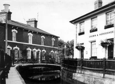 Crown and Horseshoes and New River Loop, June 1967
Exhibition caption: After replacing fencing by iron railings of a similar design to the original. The area is opened out and an impression of light and space given. The curve of the original bridge is revealed, andthe straight pipe once taking the electricity supply across the river has been relaid under the bridge surface. The cottages and their gardens are now revealed and a gate placed to indicate that their front access is not a public footpath. The public house has been repainted to an agreed colour scheme and has now become a focal point which can reflect light. The Llicensee's window boxes and tubs are now visible and the public house looks gay and inviting.
Keywords: pubs;New River Loop;railings;bridges