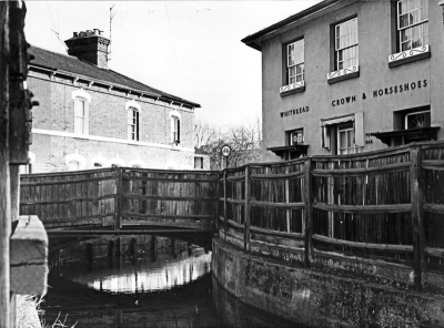Crown and Horseshoes and New River Loop, 1967
Wooden fence before improvement. Exhibition caption for this image reads "The Crown and Horseshoes through a gap in the high close-boarded fencing. Both public house and cottages are half hidden and the fencing gives the whole area a dark, neglected air. The drab rendering of the Crown and Horseshoes is dull and forbidding".
Keywords: pubs;New River Loop;bridges;1960s;fencing