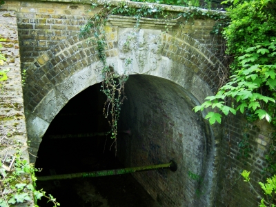 Clarendon Arch, Bush Hill
Bult in 1786, the arch ring of Portland stone bears a fine shield of arms with mantling helm and the crest of Myddelton, and the inscription "This arch is at the end of a long, barrel-vaulted brick tunnel which carries the Salmons Brook beneath the New River". Above the north-west side of the tunnel is a stone with the inscription: "This bank of earth was raised and formed to support the Channel of the New River. And the frame of timber and lead which served that purpose 173 years was removed and taken away. MDCCLXXXVI Peter Holford, Esquire, Governor". - [i]Treasures of Enfield[/i], p.119.
Keywords: New River;rivers and streams;Grade II listed;tunnels
