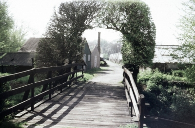 Location unknown
A bridge leading under a tree arch towards greenhouses and buildings. Can anyone say where this is?
Keywords: bridges;glasshouses;trees